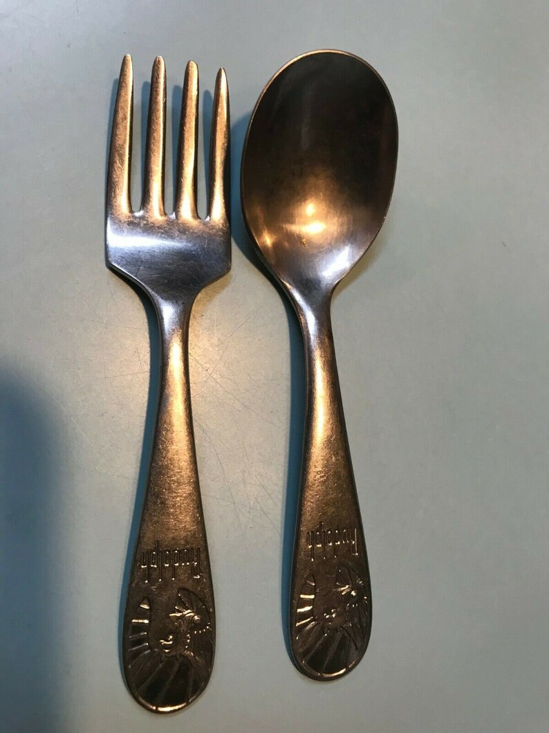 K&ouml;nnte beinhalten: Ein Vintage-Set aus Gabel und L&ouml;ffel aus Silber. Die Gabel hat vier Zinken und der L&ouml;ffel hat eine abgerundete Sch&uuml;ssel. Beide Utensilien haben ein dekoratives Design am Griff mit dem Wort "Rudolph" und einem Widderkopf.