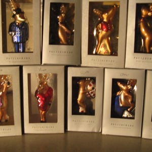 May include: A collection of glass reindeer Christmas ornaments in their original boxes. Each ornament is uniquely designed, with some wearing outfits like a blue suit or a red coat. The ornaments are in various poses.