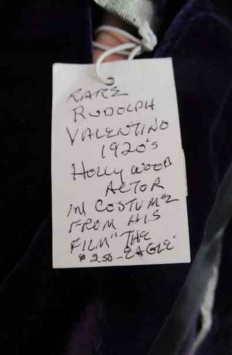 May include: A white tag with black handwritten text that reads "KARE RODOLPH VALENTINO 1920's Holly wood ACTOR in COSTUMZ FROM HIS FILM "THE 250-EAGLE"