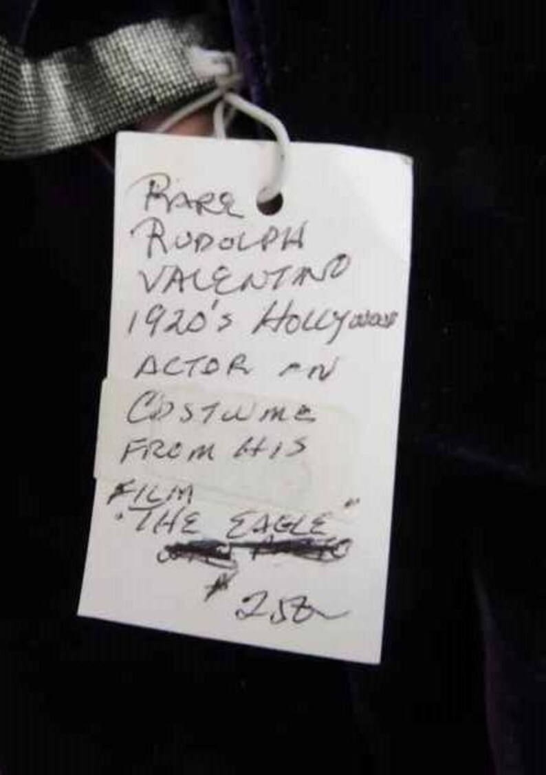 May include: A white paper tag with black handwritten text that reads "RARE RUDOLPH VALENTINO 1920's Hollywood ACTOR IN Costume FROM HIS FILM "THE EAGLE" 258".