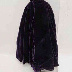 May include: A purple velvet cape with a high collar and gold buttons. The cape is worn by a doll.