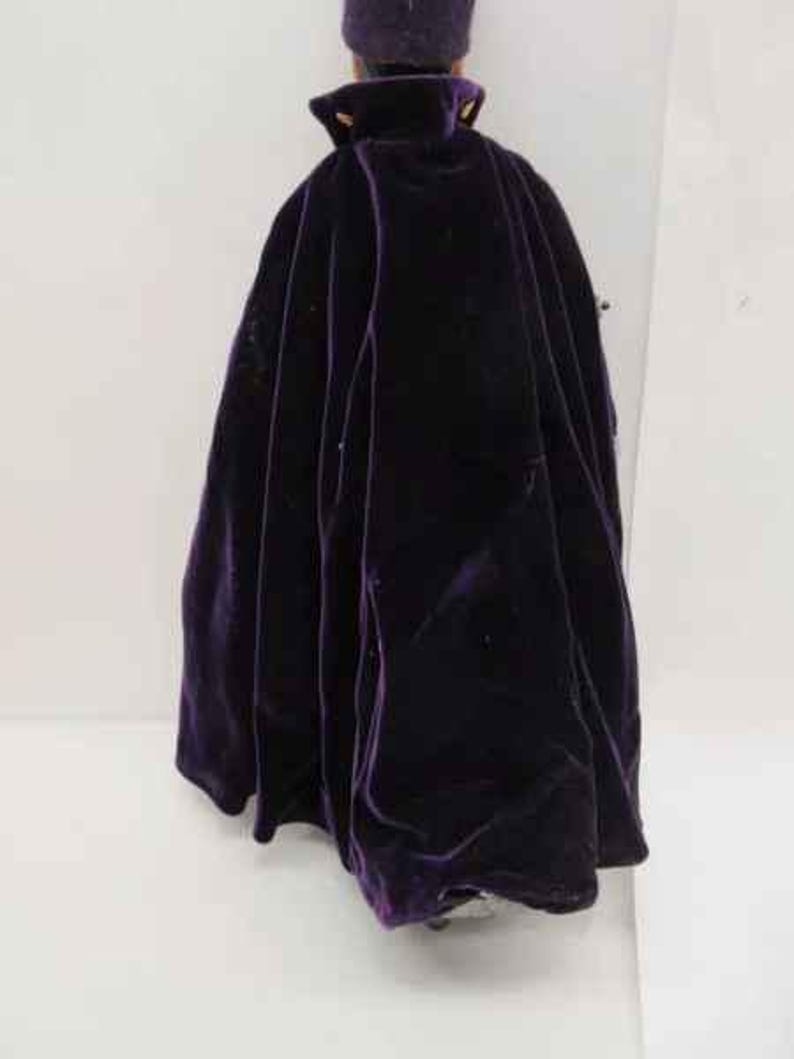 May include: A purple velvet cape with a high collar and gold buttons. The cape is worn by a doll.
