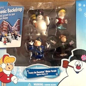 May include: A boxed Frosty the Snowman Winter Parade figurine display set. The set includes several figurines of characters from the animated film, including Frosty, a police officer, and other figures. The box features a scenic backdrop.