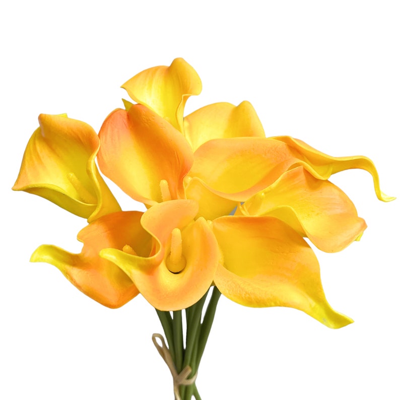 May include: A bouquet of artificial calla lilies in shades of yellow and orange. The flowers have a smooth, waxy texture and are tied together with a twine ribbon. The stems are green, and the background is white.