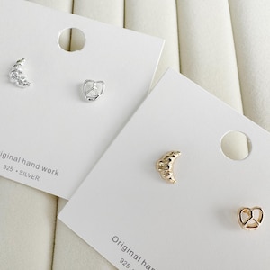 Può includere: Due carte bianche con orecchini d'argento e due carte bianche con orecchini d'oro. Gli orecchini hanno la forma di una mezzaluna e di un segno di pace. Le carte riportano il testo "Original hand work 925 - SILVER".