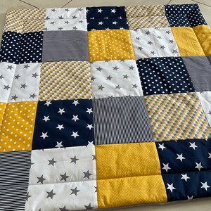 May include: A patchwork quilt featuring a range of patterns in yellow, white and navy blue. The quilt is made up of squares with different designs, including stars, polka dots and stripes.