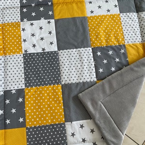 May include: A patchwork quilt featuring a grey, white and yellow star design. The quilt is made from various fabrics and has a soft, plush backing.