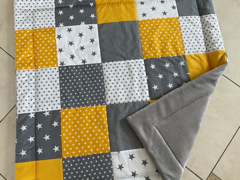 May include: A patchwork quilt featuring a grey, white and yellow star design. The quilt is made from various fabrics and has a soft, plush backing.