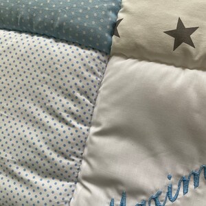 May include: A white and blue patchwork baby quilt with a blue embroidered name "Maxim" on one of the squares.