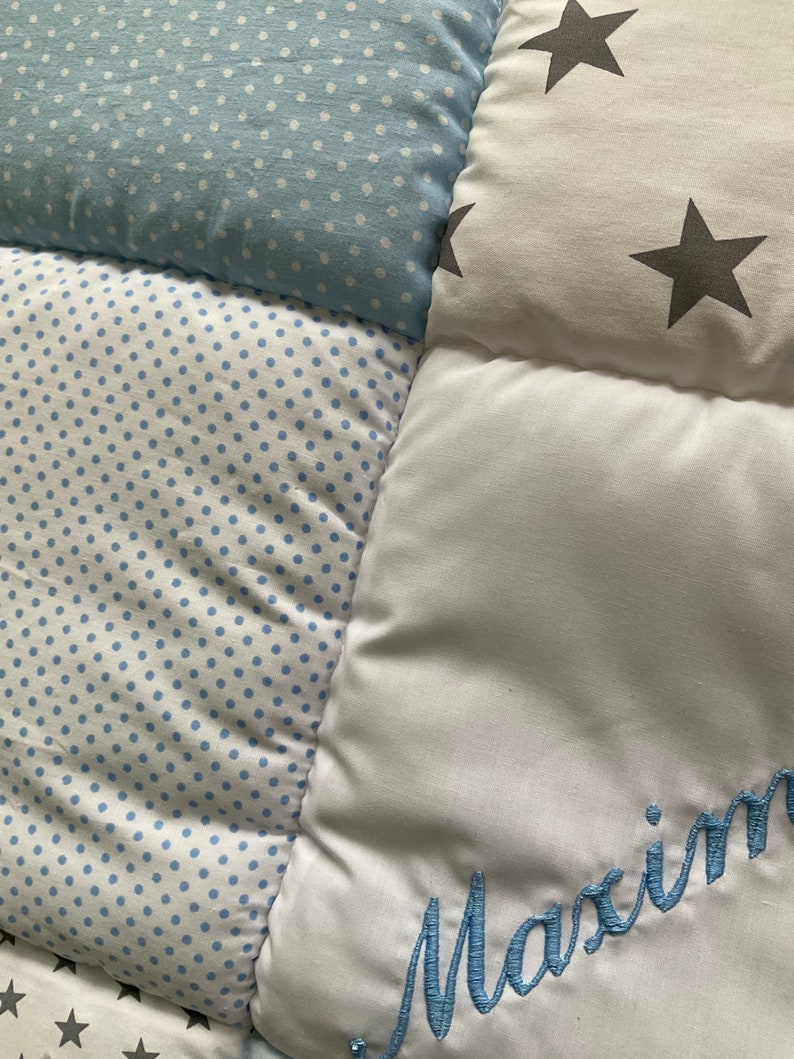 May include: A white and blue patchwork baby quilt with a blue embroidered name "Maxim" on one of the squares.
