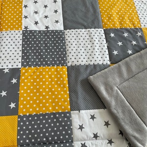 May include: A patchwork baby playmat with a soft grey fleece backing. The playmat is made of different fabrics with yellow and grey stars and polka dots.