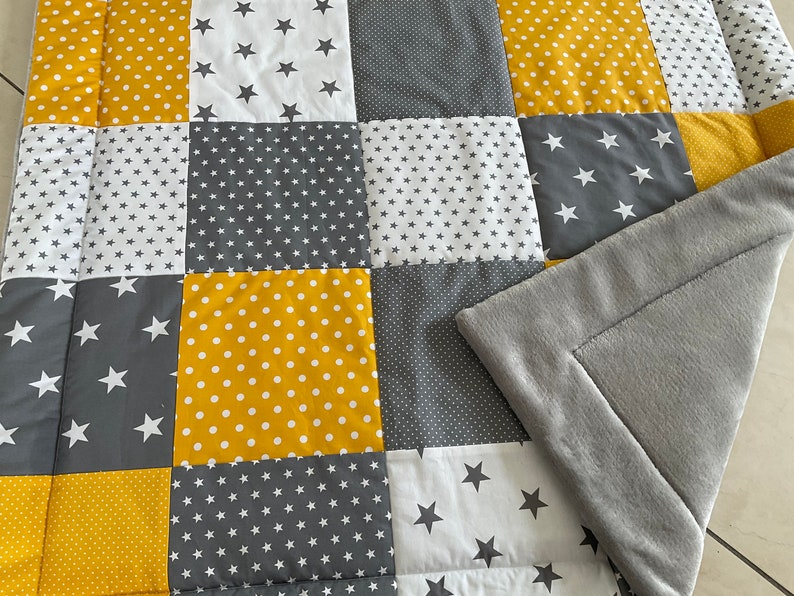 May include: A patchwork baby playmat with a soft grey fleece backing. The playmat is made of different fabrics with yellow and grey stars and polka dots.