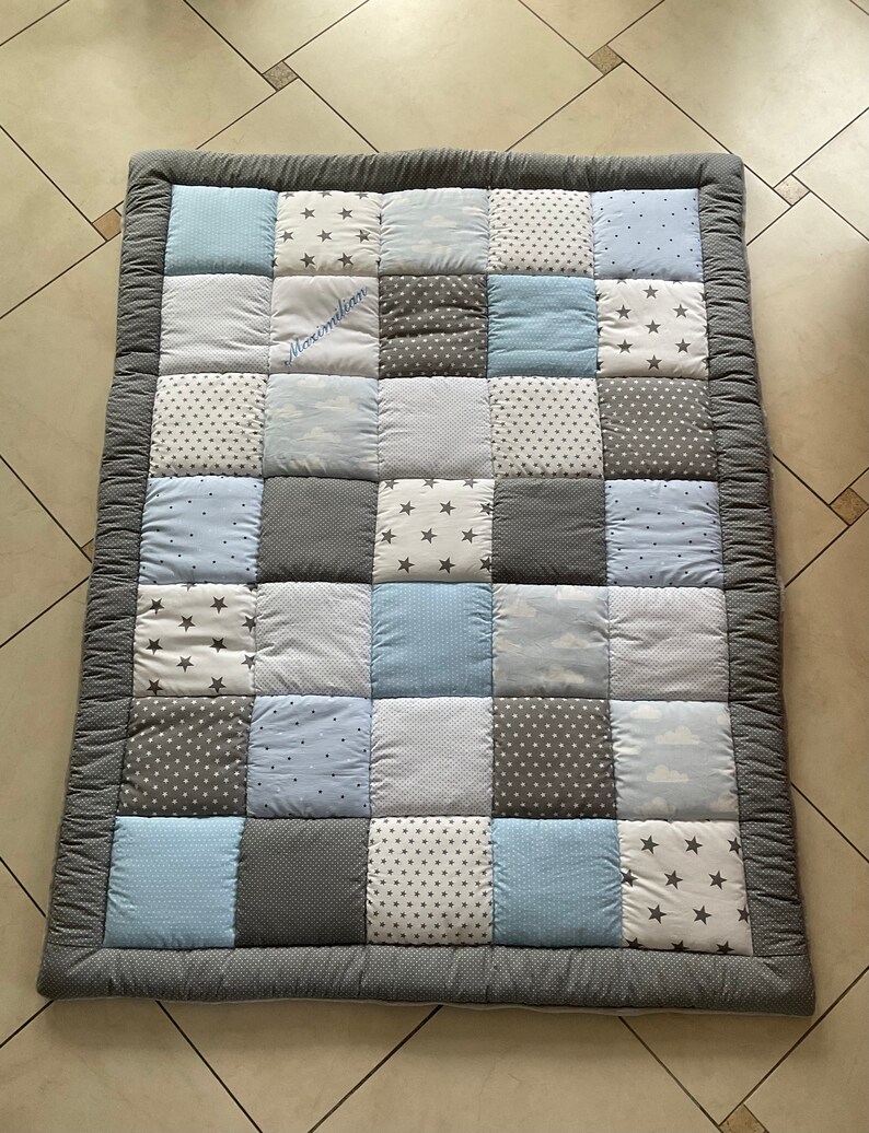 May include: A gray and blue patchwork play mat with a white star pattern and the name Maximilian embroidered on it.