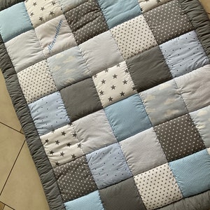 May include: A gray and blue patchwork baby quilt with a personalized name, Maximilian, embroidered in white thread.