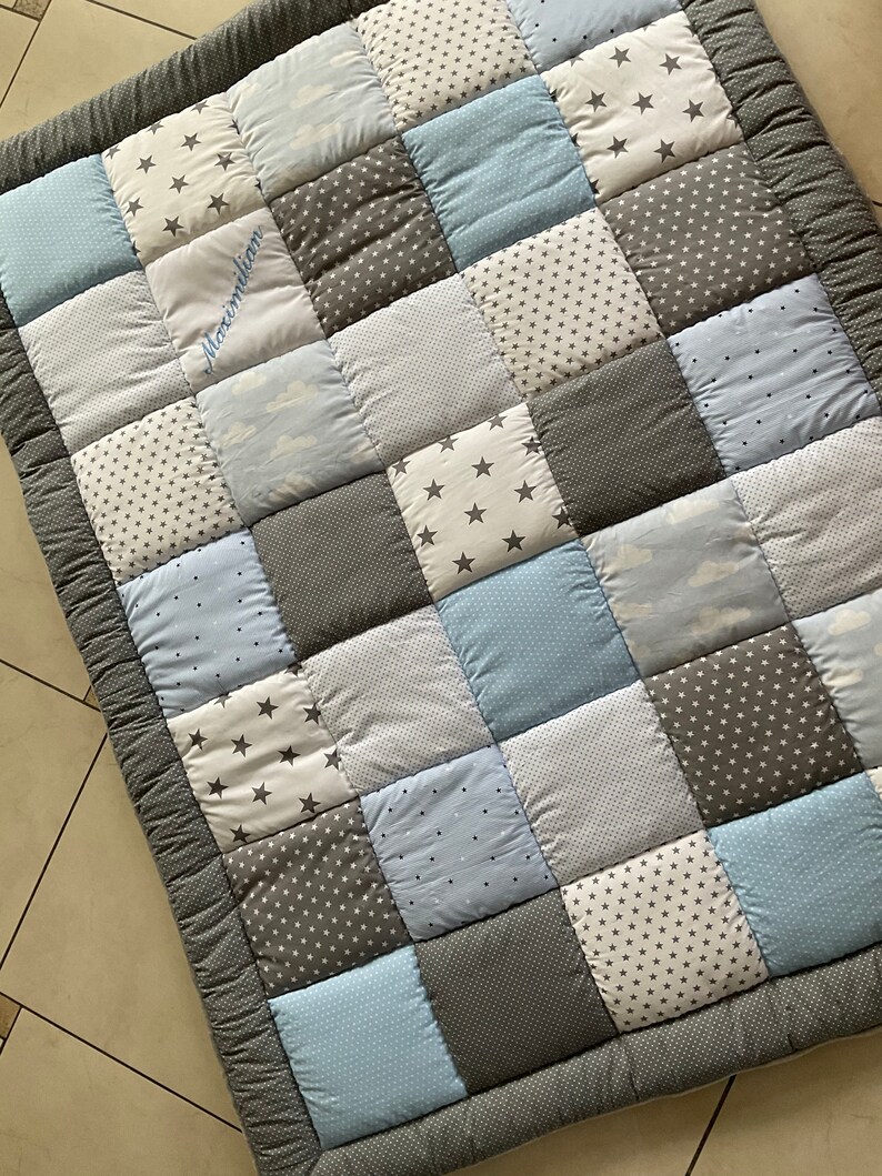 May include: A gray and blue patchwork baby quilt with a personalized name, Maximilian, embroidered in white thread.