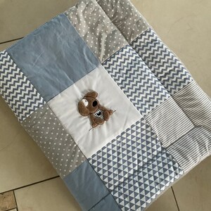 Peut inclure: Une couverture b&eacute;b&eacute; en patchwork bleu et gris avec un petit chien brun brod&eacute; au centre.