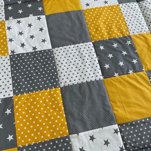 May include: A patchwork quilt featuring a mix of yellow and grey fabrics. The quilt is made up of squares with different patterns, including polka dots, stars, and small dots.