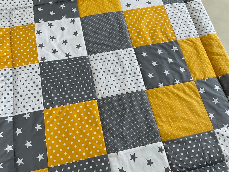 May include: A patchwork quilt featuring a mix of yellow and grey fabrics. The quilt is made up of squares with different patterns, including polka dots, stars, and small dots.