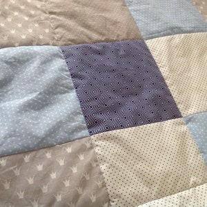 Pu&ograve; includere: Una trapunta patchwork con una variet&agrave; di motivi, tra cui corone, pois e disegni geometrici. La trapunta &egrave; realizzata in tonalit&agrave; di blu, grigio e bianco.