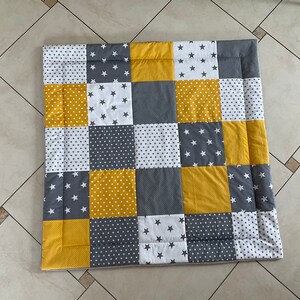 May include: A patchwork playmat in a yellow and grey colour scheme. The squares are made of different fabrics with white stars, polka dots, and solid colours.