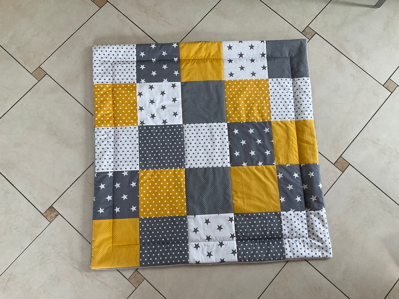 May include: A patchwork playmat in a yellow and grey colour scheme. The squares are made of different fabrics with white stars, polka dots, and solid colours.