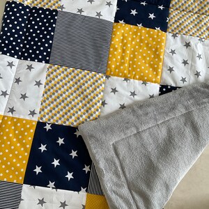 May include: A patchwork baby quilt featuring a range of yellow and navy blue patterns, including stars, polka dots, and stripes. The quilt is made from soft, comfortable fabric and is ideal for snuggling.