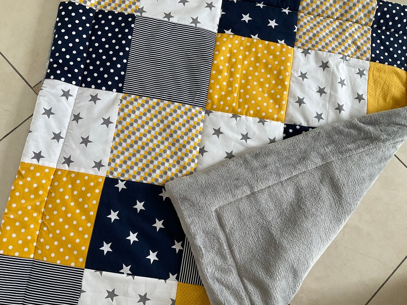 May include: A patchwork baby quilt featuring a range of yellow and navy blue patterns, including stars, polka dots, and stripes. The quilt is made from soft, comfortable fabric and is ideal for snuggling.