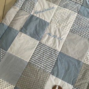 Peut inclure: Une courtepointe b&eacute;b&eacute; en patchwork bleu et blanc avec le nom "Constantin" et la date "16.12.21" brod&eacute;s dessus.