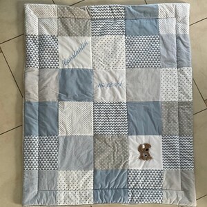 Peut inclure: Une courtepointe b&eacute;b&eacute; patchwork bleu et gris avec un chien brod&eacute; blanc et le texte "Constantijn 16.12.24".