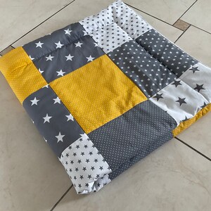 May include: A patchwork quilt with a yellow, grey, and white star pattern. The quilt is made of different fabrics and is folded in half.