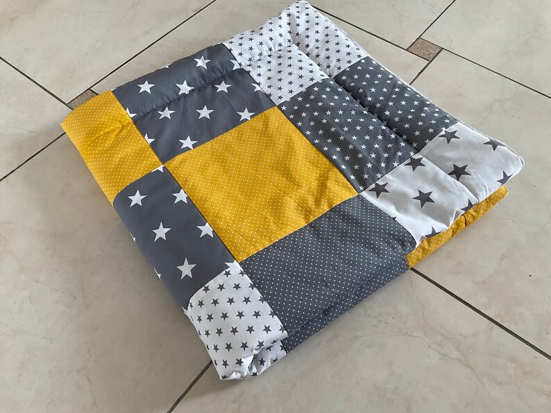 May include: A patchwork quilt with a yellow, grey, and white star pattern. The quilt is made of different fabrics and is folded in half.