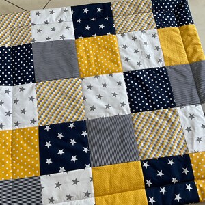 May include: A patchwork baby quilt with squares of yellow, white and navy blue fabric. Some squares have white polka dots, some have grey and yellow checkered patterns, and some have white stars on a navy blue background.