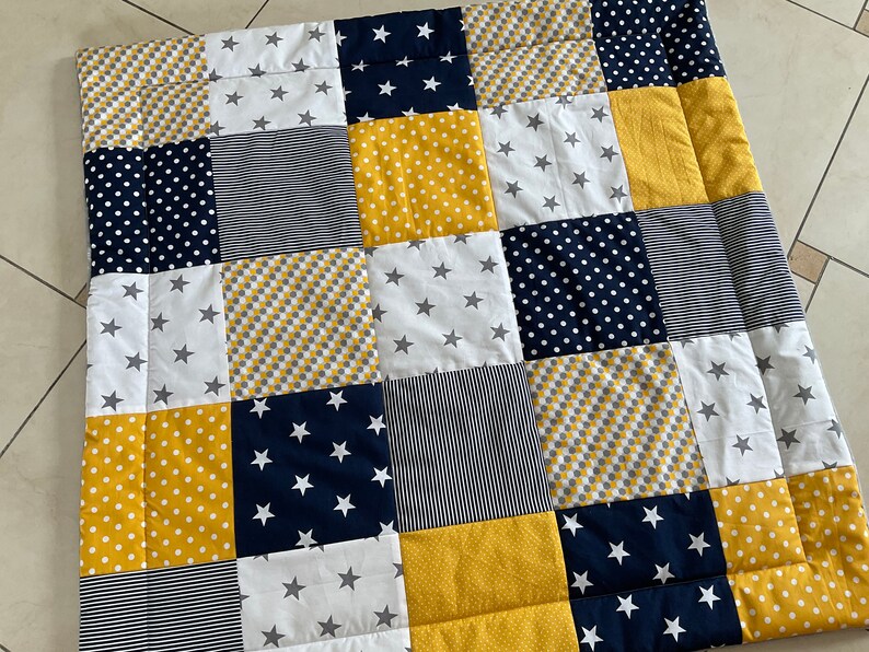 May include: A patchwork baby quilt with squares of yellow, white and navy blue fabric. Some squares have white polka dots, some have grey and yellow checkered patterns, and some have white stars on a navy blue background.