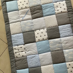 May include: A gray and blue patchwork baby quilt with a white embroidered name "Maximilian".