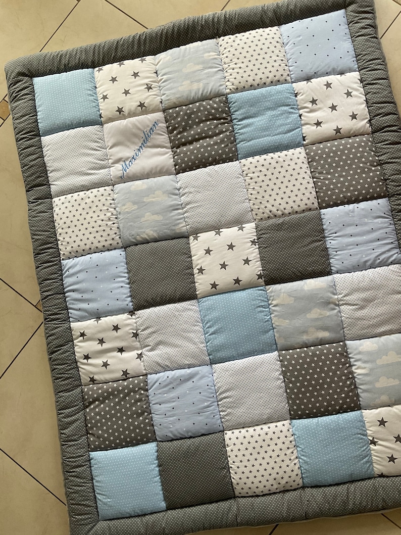 May include: A gray and blue patchwork baby quilt with a white embroidered name "Maximilian".