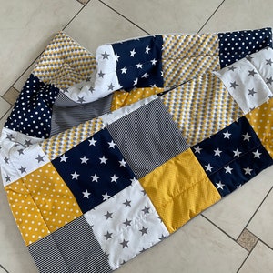 May include: A patchwork quilt featuring a mix of yellow, navy blue, white and grey fabrics. The quilt is made up of squares with different patterns, including polka dots, stripes and stars.