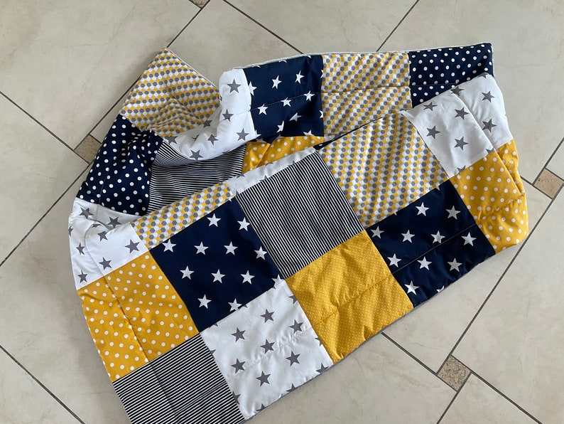 May include: A patchwork quilt featuring a mix of yellow, navy blue, white and grey fabrics. The quilt is made up of squares with different patterns, including polka dots, stripes and stars.