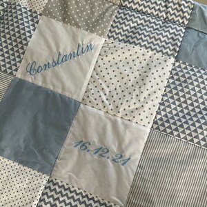 Peut inclure: Une courtepointe b&eacute;b&eacute; en patchwork bleu et blanc avec le nom "Constantin" et la date "16.12.24" brod&eacute;s dessus.
