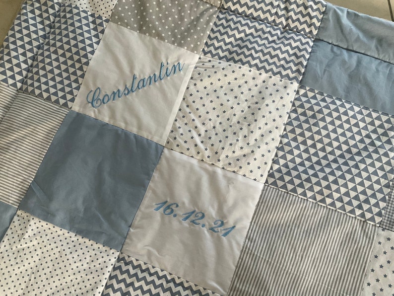 Peut inclure: Une courtepointe b&eacute;b&eacute; en patchwork bleu et blanc avec le nom "Constantin" et la date "16.12.24" brod&eacute;s dessus.