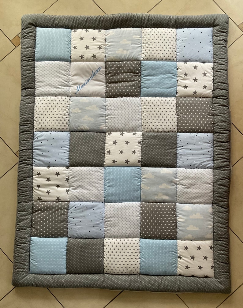 May include: A gray and blue patchwork baby playmat with a white embroidered name "Maximilian".
