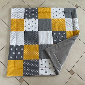 May include: A grey and yellow patchwork baby play mat with a soft grey fleece backing. The mat is made of different fabrics with various patterns, including stars, polka dots, and solid colours.