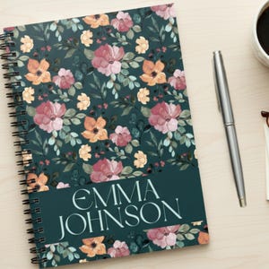 May include: A spiral-bound notebook with a floral design. The cover features a dark teal background with pink, orange, and yellow flowers and green leaves. The name "EMMA JOHNSON" is printed in white. A pen, coffee cup, glasses, and notepad are also visible.