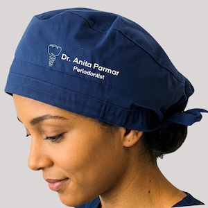 May include: A navy blue surgical scrub cap with a white dental graphic and text. The text reads "Dr. Anita Parmar, Periodontist". The cap is tied at the back.