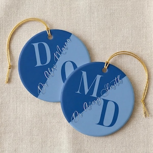 May include: Two blue and light blue ceramic ornaments with gold string hangers. Each ornament features a large letter and the name "Dr. Alex Mason" or "Dr. Avery Smith" in a script font.