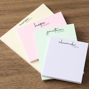 May include: Four rectangular paper notepads in pastel yellow, pink, light green, and white. Each pad features custom black printed text: marissa CLASS MOM, hope FOR LIFE, jonathan STILERNO, and alexander MARTIN, arranged in a layered, overlapping stack.