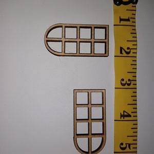 Könnte beinhalten: Zwei hölzerne Fensterschnitte, einer mit einem gewölbten Oberteil und der andere mit einem abgerundeten Unterteil, beide mit einem Raster aus neun Quadraten. Die Ausschnitte sind etwa 5 cm hoch und befinden sich neben einem gelben Maßband.