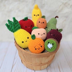 May include: A wooden basket filled with crocheted fruit, including a pineapple, apple, banana, orange, peach, pear, kiwi, and a plum. The fruit are all smiling and have googly eyes.