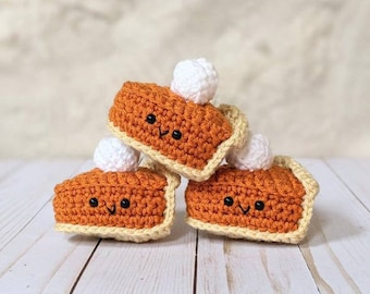 May include: Three crocheted pumpkin pie plush toys with smiling faces. The pies are stacked on top of each other, with the top pie having a white crocheted dollop of whipped cream.