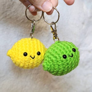 May include: Two crochet keychains: a yellow lemon and a green lime, each with a smiling face and attached to a metal keyring. The lemon is a bright yellow, and the lime is a vibrant green.