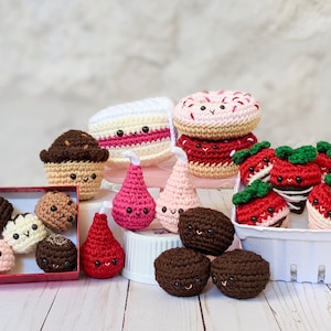 Könnte beinhalten: Eine Sammlung von gehäkelten Plüschtieren mit Lebensmittel-Motiven, darunter ein Donut, ein Kuchen, ein Cupcake, Erdbeeren und Birnen. Die Plüschtiere haben lächelnde Gesichter und sind auf einer weißen Oberfläche angeordnet.